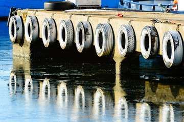 Fototapeta na wymiar Row of white painted car tires hanging as bumpers or fenders on quayside. Icy water below reflects the tires.