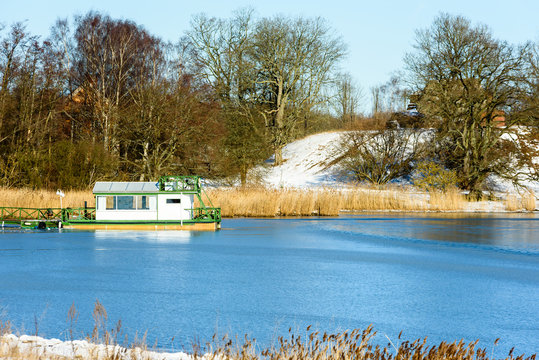 Small green and white floating cabin moored at a jetty in winter landscape with forest and a small hill in the background. Location Solvesborg, Blekinge, Sweden.