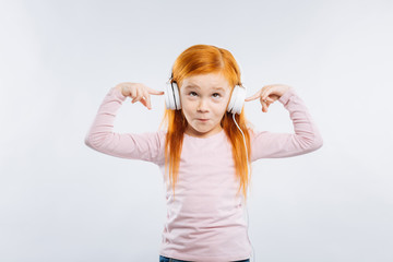 Making faces. Red-haired kid raising eyebrows and looking upwards while touching headphones