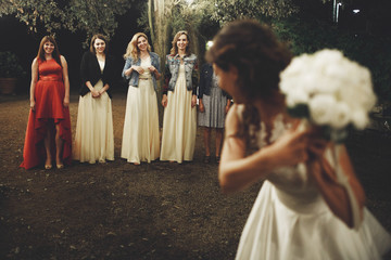 Bride stands with wedding bouquet before their friends ready to throw it