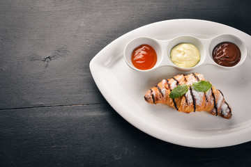 Croissant with sweet sauces. Chocolate, Vanilla and Peach. On a wooden background. Top view.