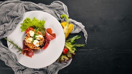 Salad with prosciutto, quail eggs, prunes and fresh vegetables on the plate. On a wooden background. Top view. Free space for text.