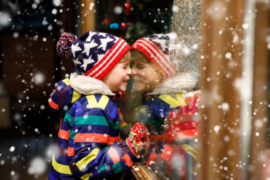 Funny Happy Child In Fashion Winter Clothes Making Window Shopping Decorated With Gifts, Xmas Tree