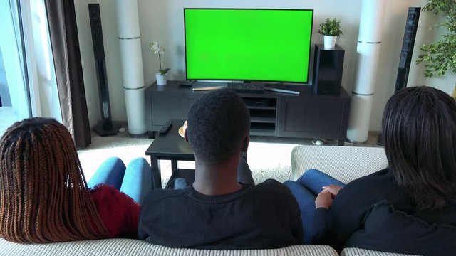 Three african friends watch television in living room - green screen 