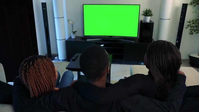 Three african friends watch television in living room and they hold around shou.