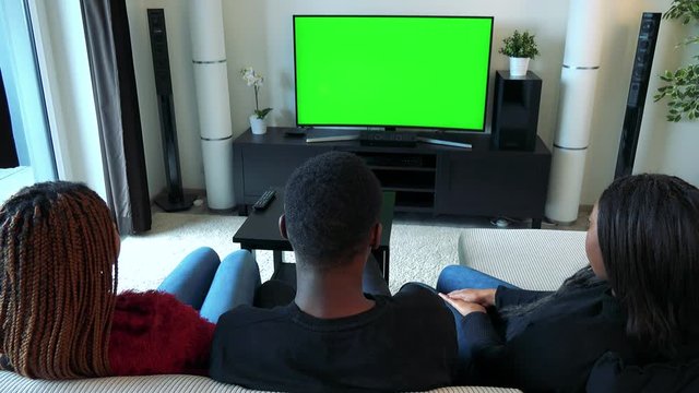 Three african friends watch television in living room and then smile to camera