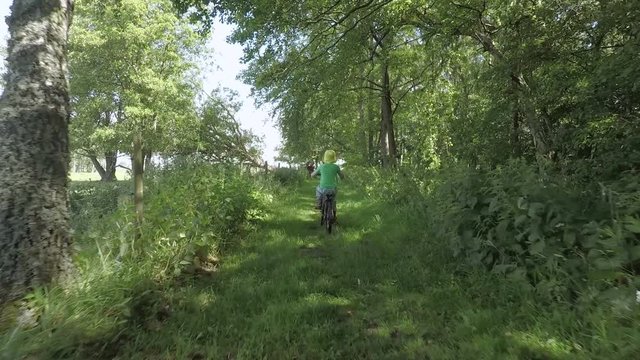 Little girl riding bicycle in green forest. Summer lifestyle moment of a happy childhood.