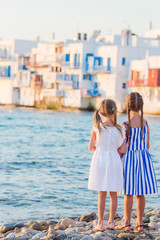 Fototapeta na wymiar Adorable little girls at Little Venice the most popular tourist area on Mykonos island, Greece. Back view of beautiful kids look at Little Venice background.