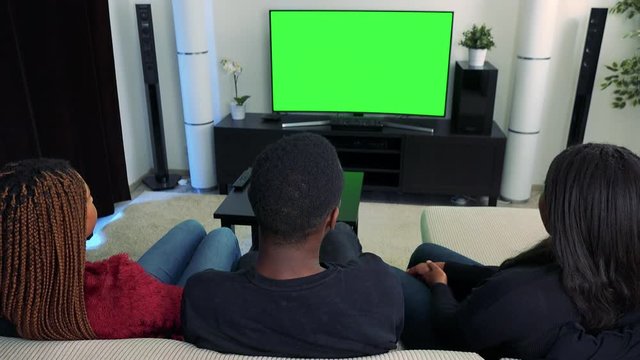Three african friends watch television and then they talk to camera