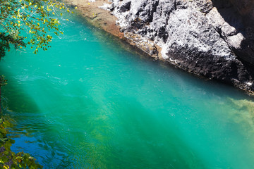 Sunlit emerald whitewater of mountain river with rocky bank