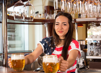Young cheerful happy bartender girl offering two beers to customers.