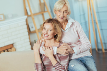 Friendly atmosphere. Positive joyful senior woman feeling peaceful and happy while being at home and hugging her smart beautiful young granddaughter