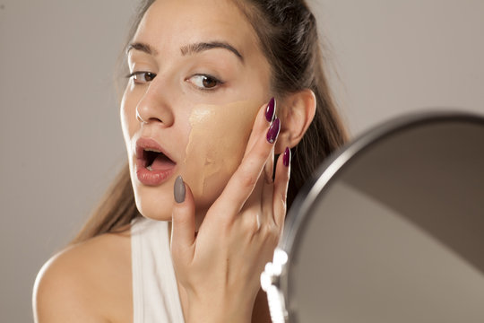 Fototapeta young woman applying a liquid foundation on her face with her fingers