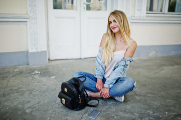 Blonde girl wear on jeans with backpack posed against old door.