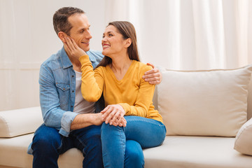 Family time. Joyful attractive nice couple  relaxing on the sofa  and cuddling each other while ...