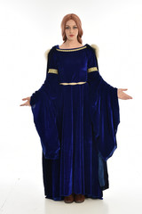 Naklejka premium full length portrait of girl wearing long blue velvet gown and fur lined cloak, standing pose on white background.