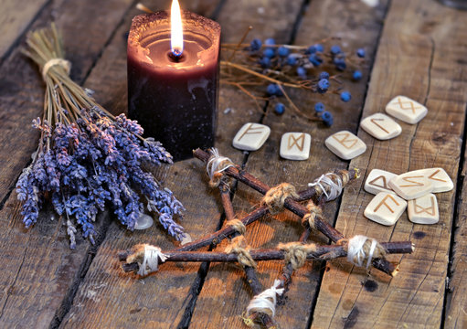 Pentagram with lavender flowers, old runes and black candle on planks. Occult, esoteric, divination and wicca concept. Mystic and vintage background