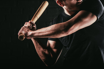 partial view of young sportsman playing baseball with bat isolated on black