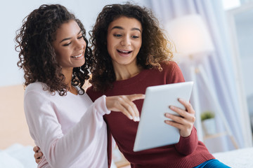 Check this out. Emotional young ladies smiling and looking at a tablet computer while spending their free time together and discussing something.