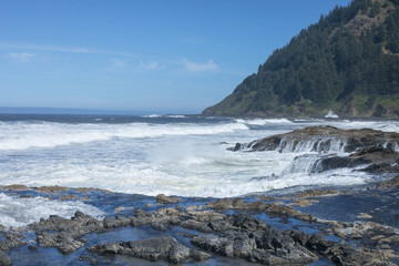Fototapeta na wymiar Beach on the Oregon Coast with waves, white water, mountain, rocks and tide pools against a blue sky