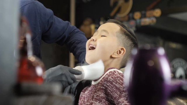 barber in black gloves makes a hairstyle for an Asian child, removes cut-off hair from the neck with a brush 60 fps