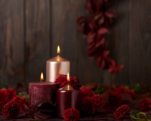 Three candles of crimson and pink color on a dark background with cones, leaves and daisies.