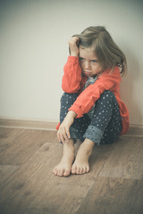 Fototapeta premium Beautiful little girl sitting on the floor. Disappointment, sadness, melancholy concept