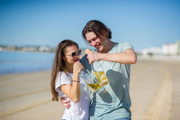 Cheerful young couple drinks wine on the beach.