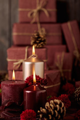 Three candles of crimson and pink color on the background of gift boxes with cones, leaves and daisies.