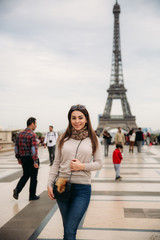 Beautiful girl posing to the photographer against the background of the Eiffel Tower. Autumn photosession. Sunny weather. Beautiful smile and makeup