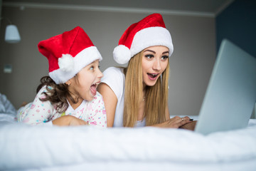Excited and surprise mother and daughter on Christmas morning using laptop in the bed