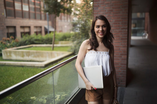 Portrait of young smiling woman holding laptop