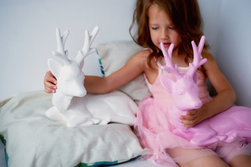 A lovely little girl 4 years old in a pink dress plays with pink deer. The atmosphere of childhood