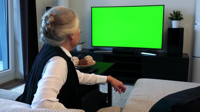 Old caucasian woman watches television in living room and then disagrees 