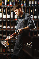 Bartender pours red wine in transparent vessel in cellar