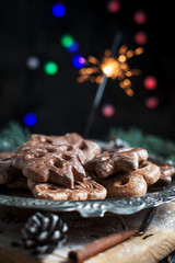 gingerbread cookies for the new year on a silver tray, New Year's lights, fireworks, fur-tree, cones, cinnamon on a wooden cutting board on a dark background