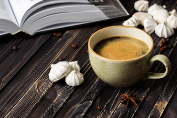 A cup of coffee with meringues and a book on a wooden background