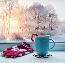 Winter background - cup with candy cane on windowsill and winter forest outdoors