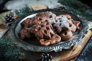 gingerbread cookies for the new year and Christmas on a silver tray, Christmas tree, cones, cinnamon on a wooden cutting board on a dark background