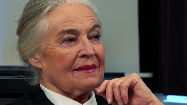 Old caucasian woman watches television in living room - closeup face