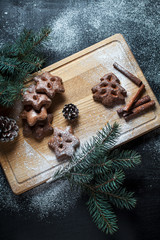 gingerbread cookies for the new year and Christmas, Christmas tree, cones, cinnamon on a wooden cutting board on a dark background