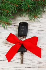 Car key with red ribbon bow on white natural wooden table background. Christmas or Valentine's Day...