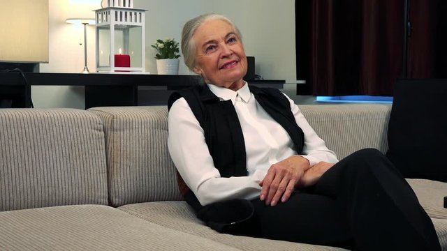 Old happy caucasian woman is thoughtful in living room 