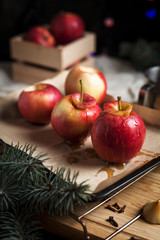 cooking of baked apples for New Year's holidays, Christmas tree and New Year's lights, honey and cinnamon on a wooden cutting board on a dark background