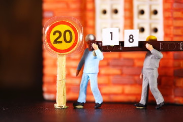 Pieces of paper during construction worker figure carrying number meaning and represent new year 2018 with miniature plastic model as a background.