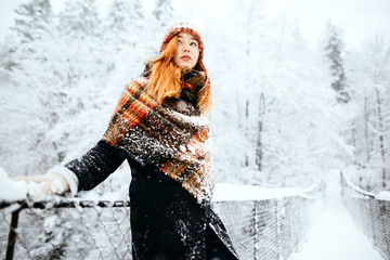 Fototapeta na wymiar Young woman winter portrait. Beautiful model girl with shiny red long hair. Young woman on suspension bridge