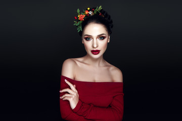 Beautiful woman portrait with red and yellow berries on head and with black hair and red lips.