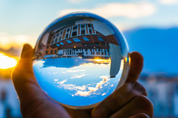 A hand holding a crystal ball for optical illusion. City as the background. Known as an orbuculum,...