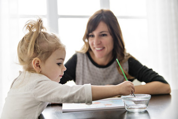 Mother and daughter painting together at home with paintbrushes and watercolors