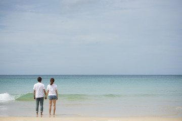 Fototapeta na wymiar Young asian couple hold hand together stand on beach look to the sea on sunny day
